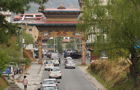 Street view of Norzin Lam in Thimphu, Bhutan, featuring traditional Bhutanese architecture, cars along the road, and lush green trees