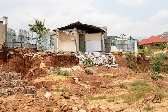A damaged house on the edge of a steep eroded slope in Bujumbura, Burundi, with exposed soil and partially collapsed structures, highlighting the impact of soil erosion.