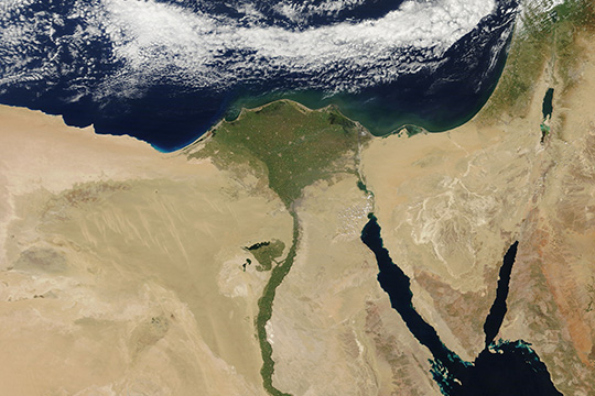 A satellite image of Egypt showing the lush green Nile River and its delta contrasting with the surrounding vast desert areas, bordered by the Mediterranean Sea and the Red Sea.